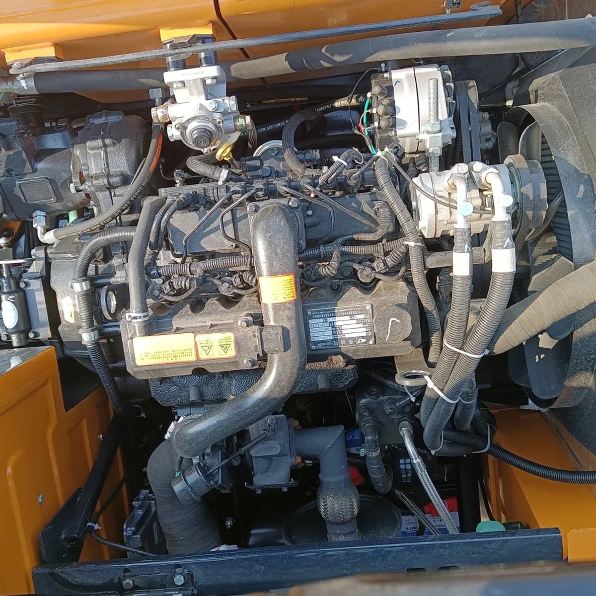 Close-up of a mini excavator diesel engine bay showing the injection pump, wiring harness, and hydraulic lines