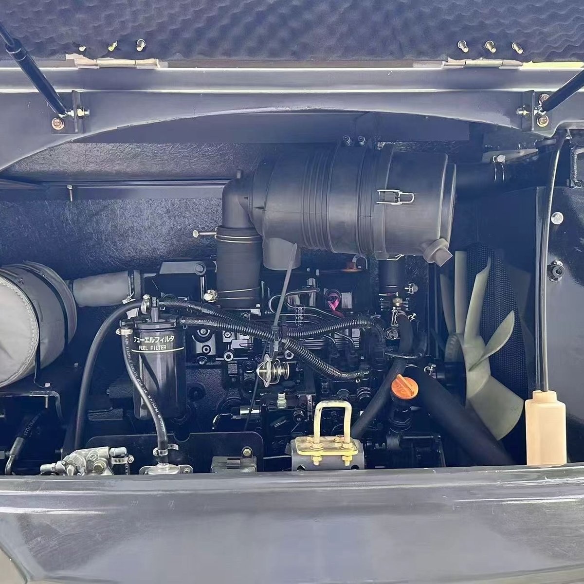 Mini excavator engine bay with service cover raised showing fuel filter and engine components