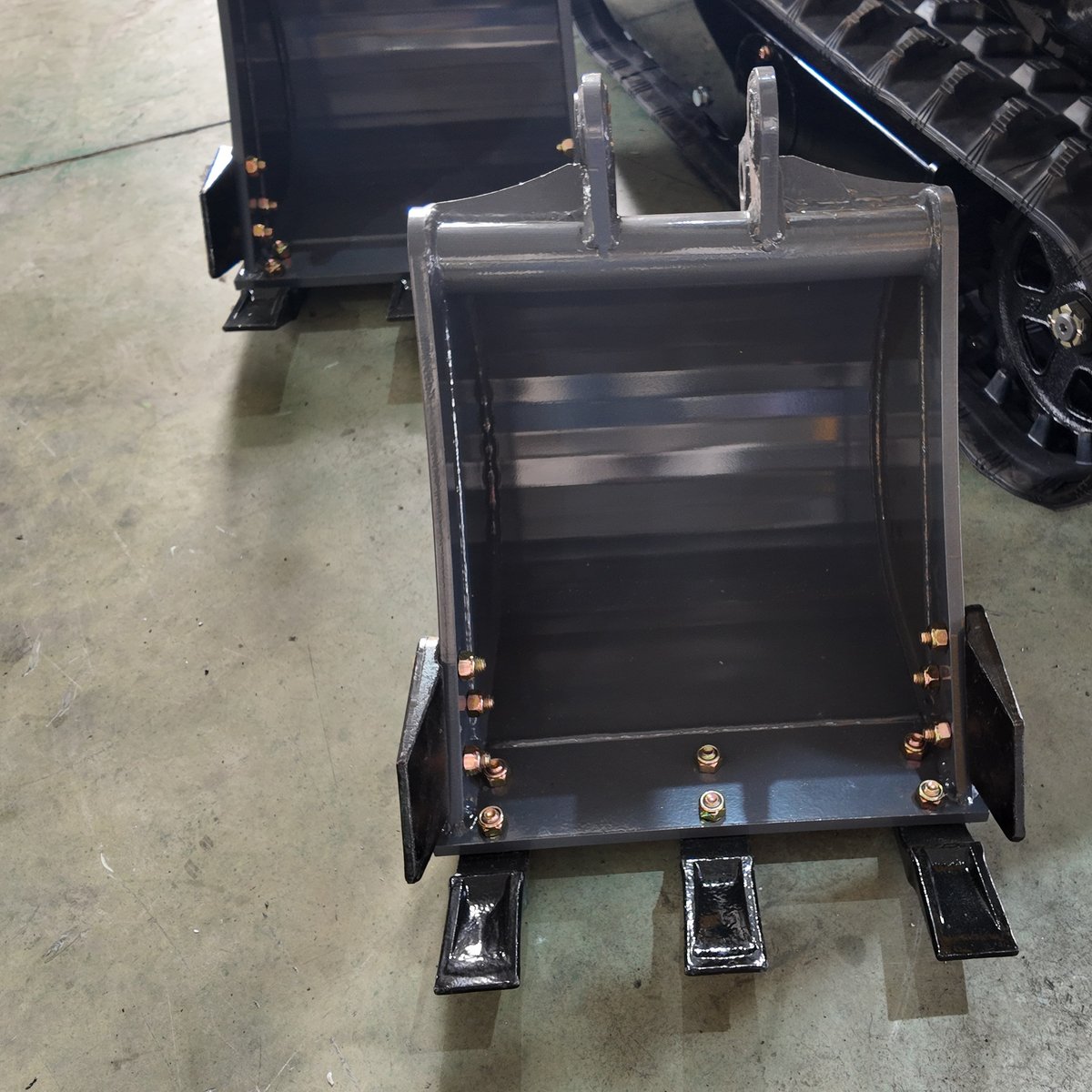 Mini excavator trenching bucket with teeth alongside a wider bucket at the factory