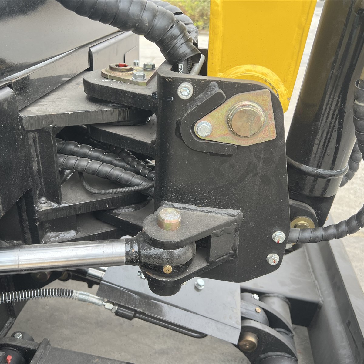Close-up of a mini excavator boom swing pivot showing the vertical pivot assembly, hydraulic cylinder and hoses