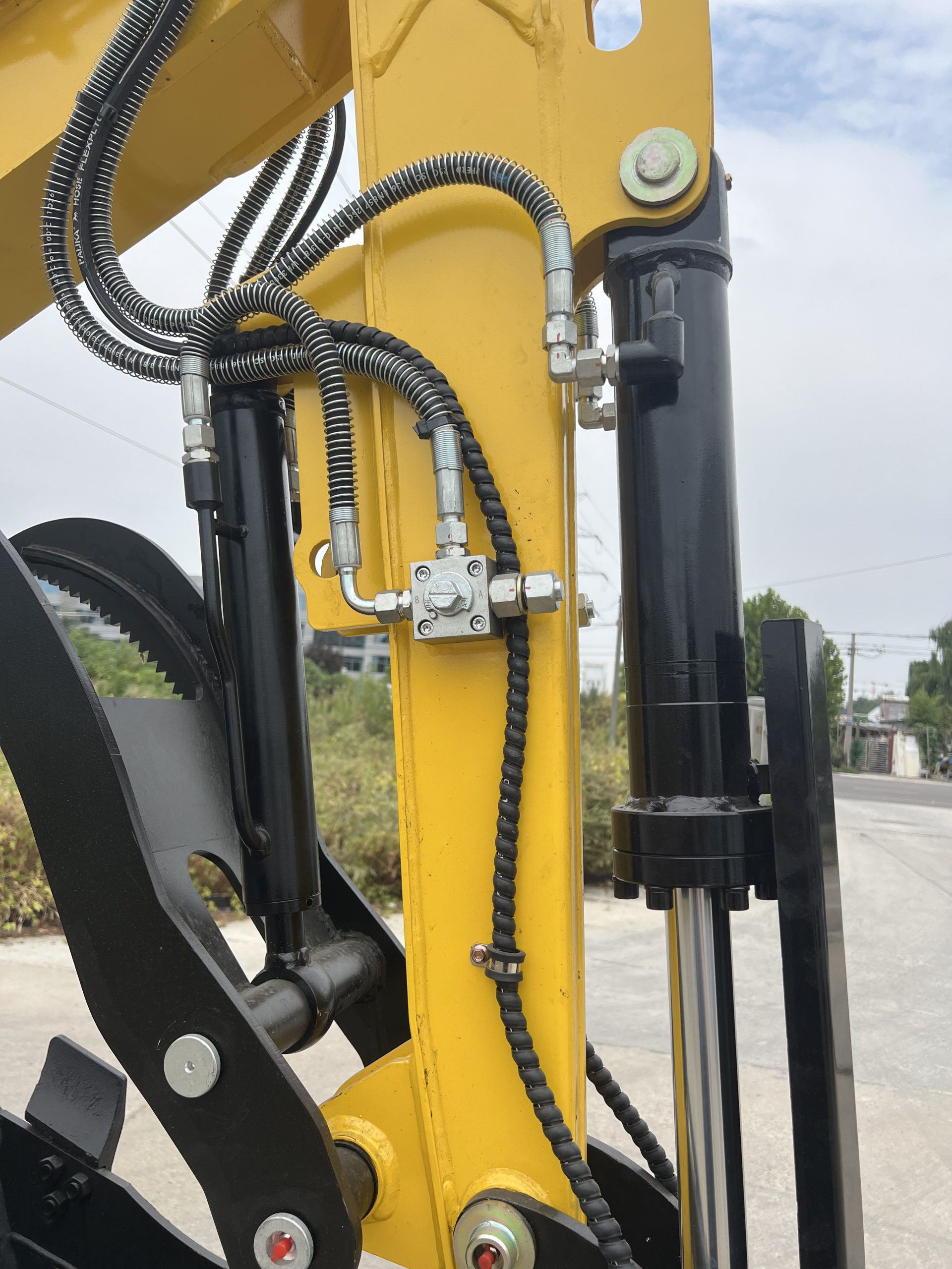 Hydraulic hoses, fittings and cylinders photographed along a yellow mini excavator arm