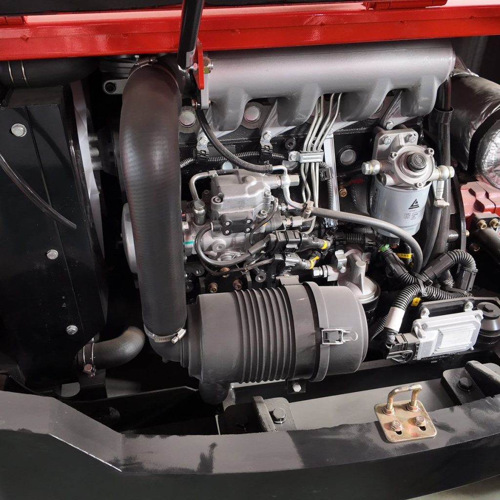 Open engine compartment on a red compact construction machine with hoses, filters and air cleaner visible