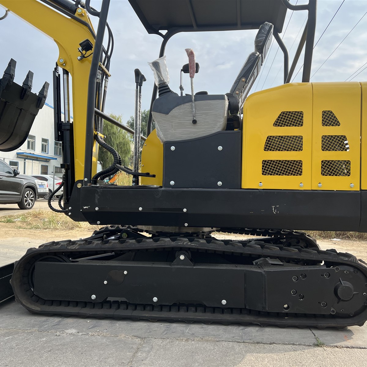 Side detail of a yellow mini excavator showing the operator station and rear body above the rubber tracks